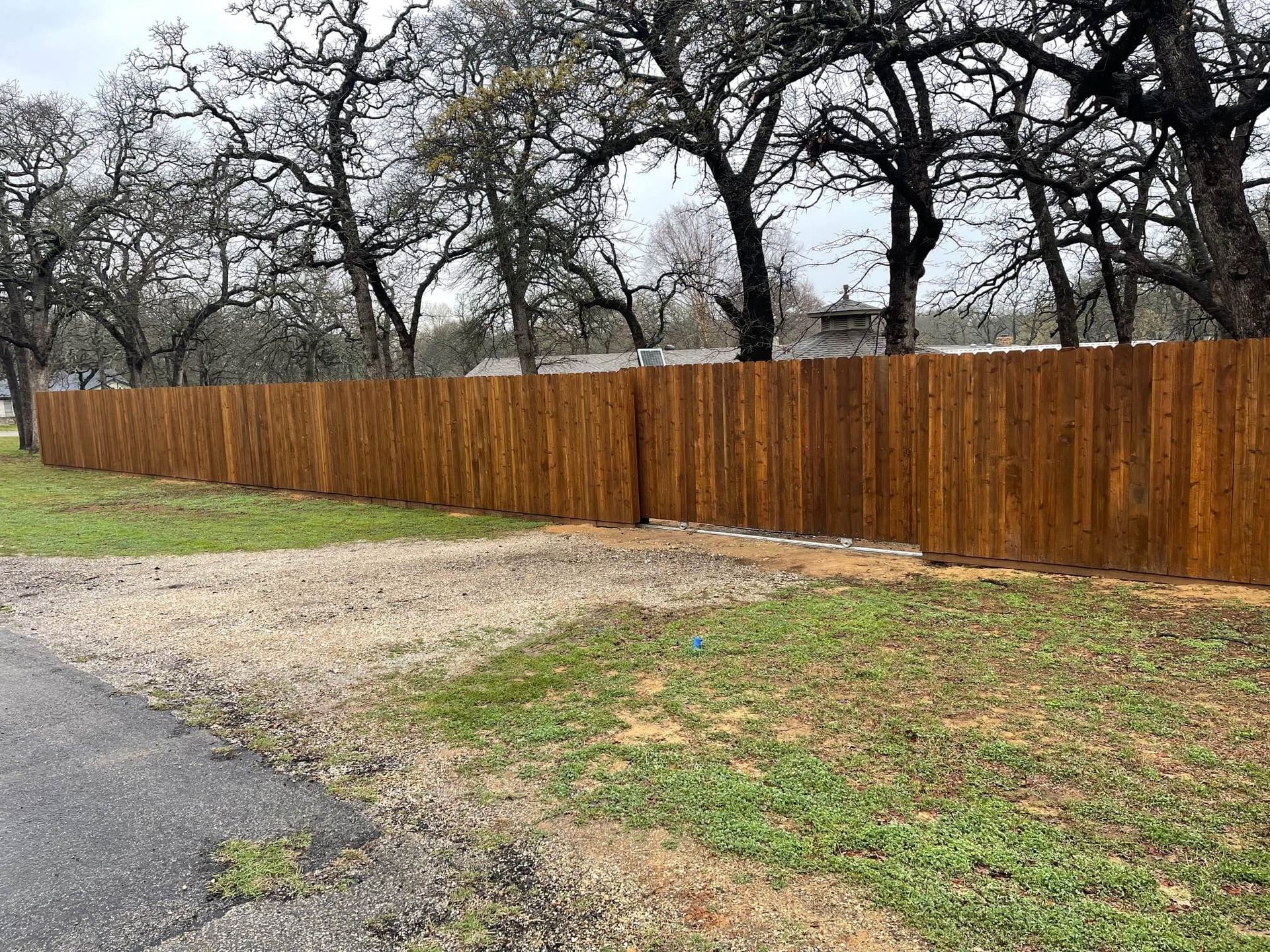 A Wooden Fence Surrounds a Grassy Field with Trees in The Background