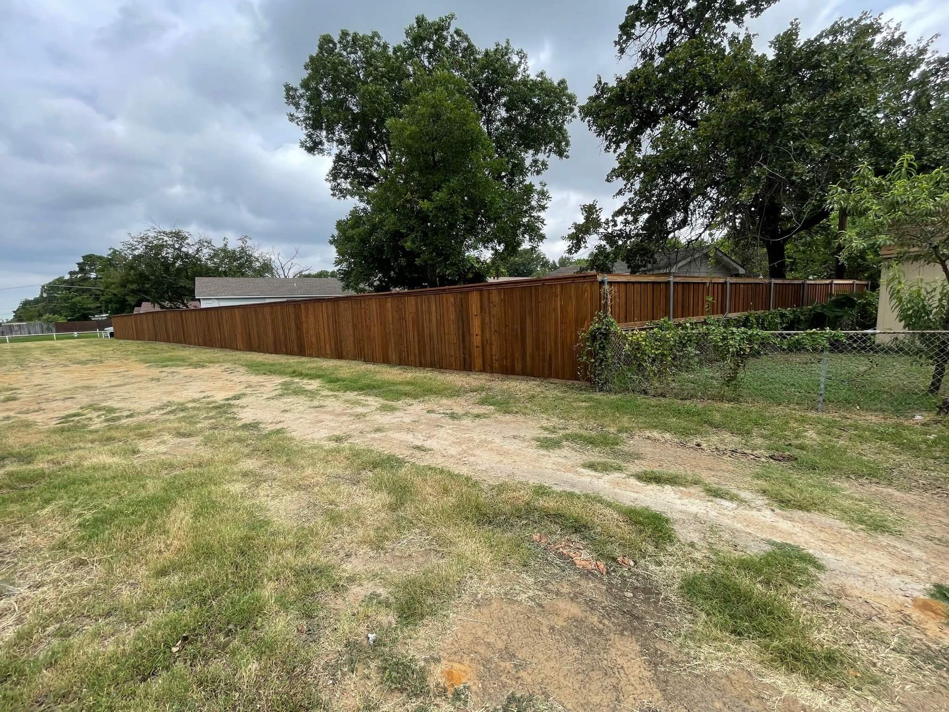 A Wooden Fence Surrounds a Grassy Field with Trees in The Background