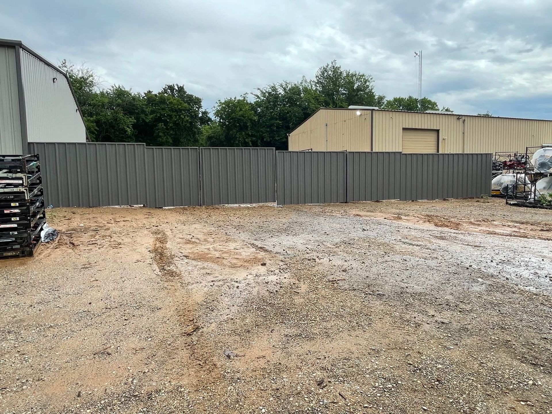 A Gravel Lot with A Fence and A Building in The Background
