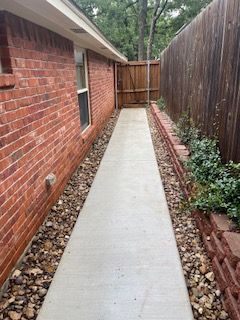 Brick House with A Wooden Fence and A Concrete Walkway Leading to It