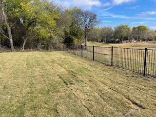 Fence Surrounds a Lush Green Field with Trees in The Background