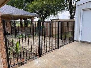 Black Wrought Iron Fence Is Surrounding a Concrete Driveway in Front of A House