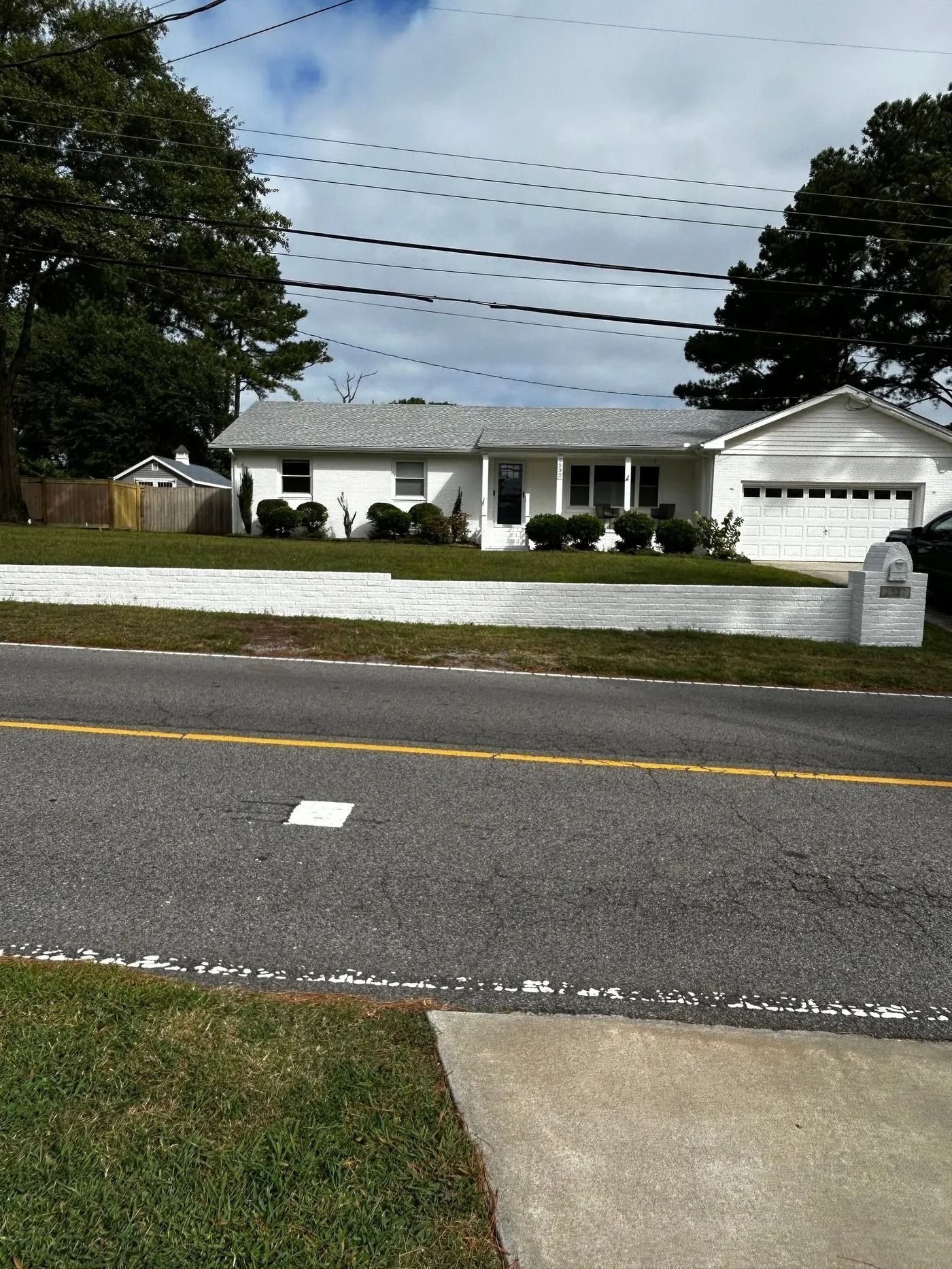 White house with a gray roof, white wall, and green lawn. Trees and power lines in the background.