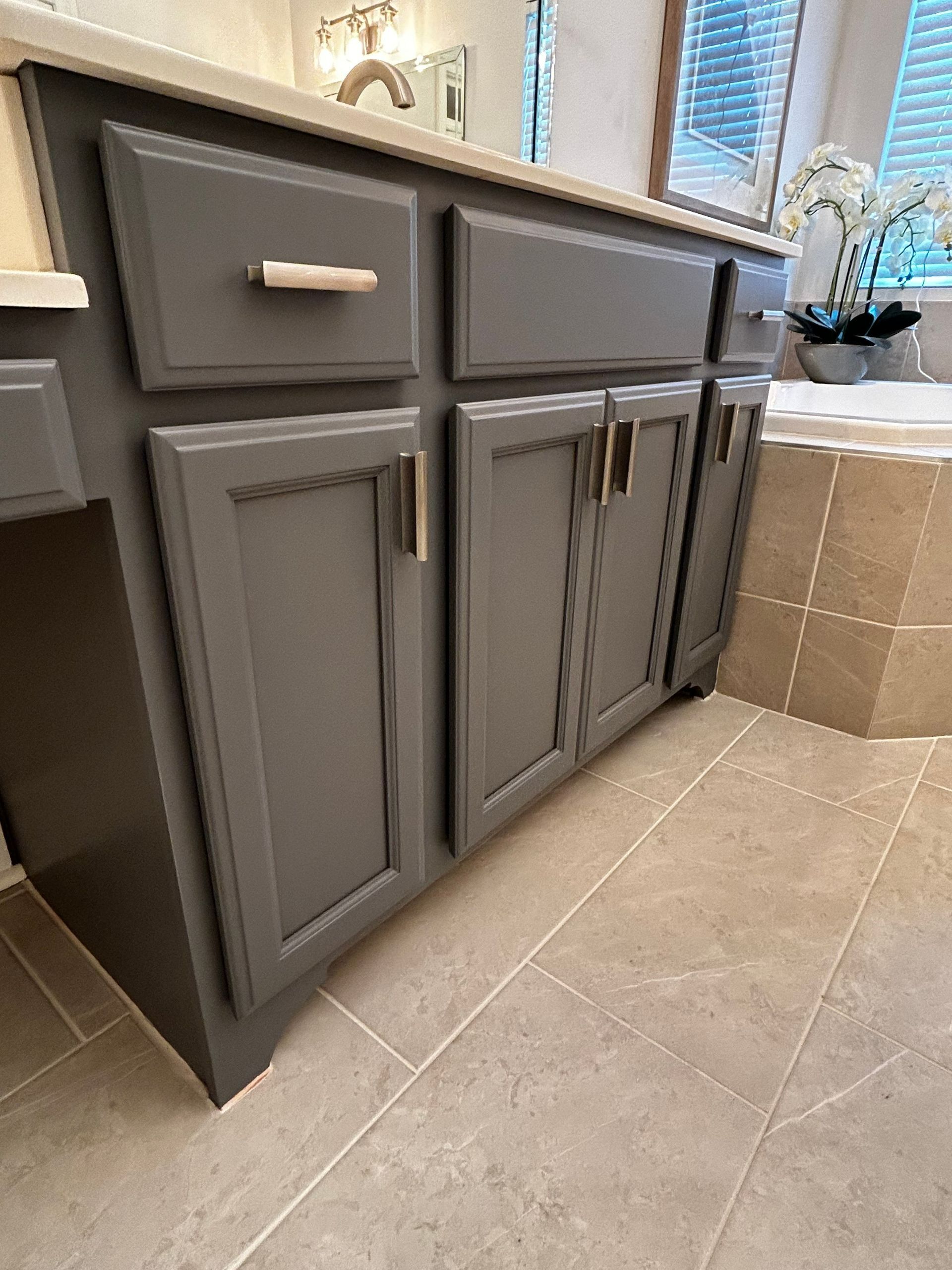Gray bathroom vanity with gold hardware, sitting on a light tile floor.