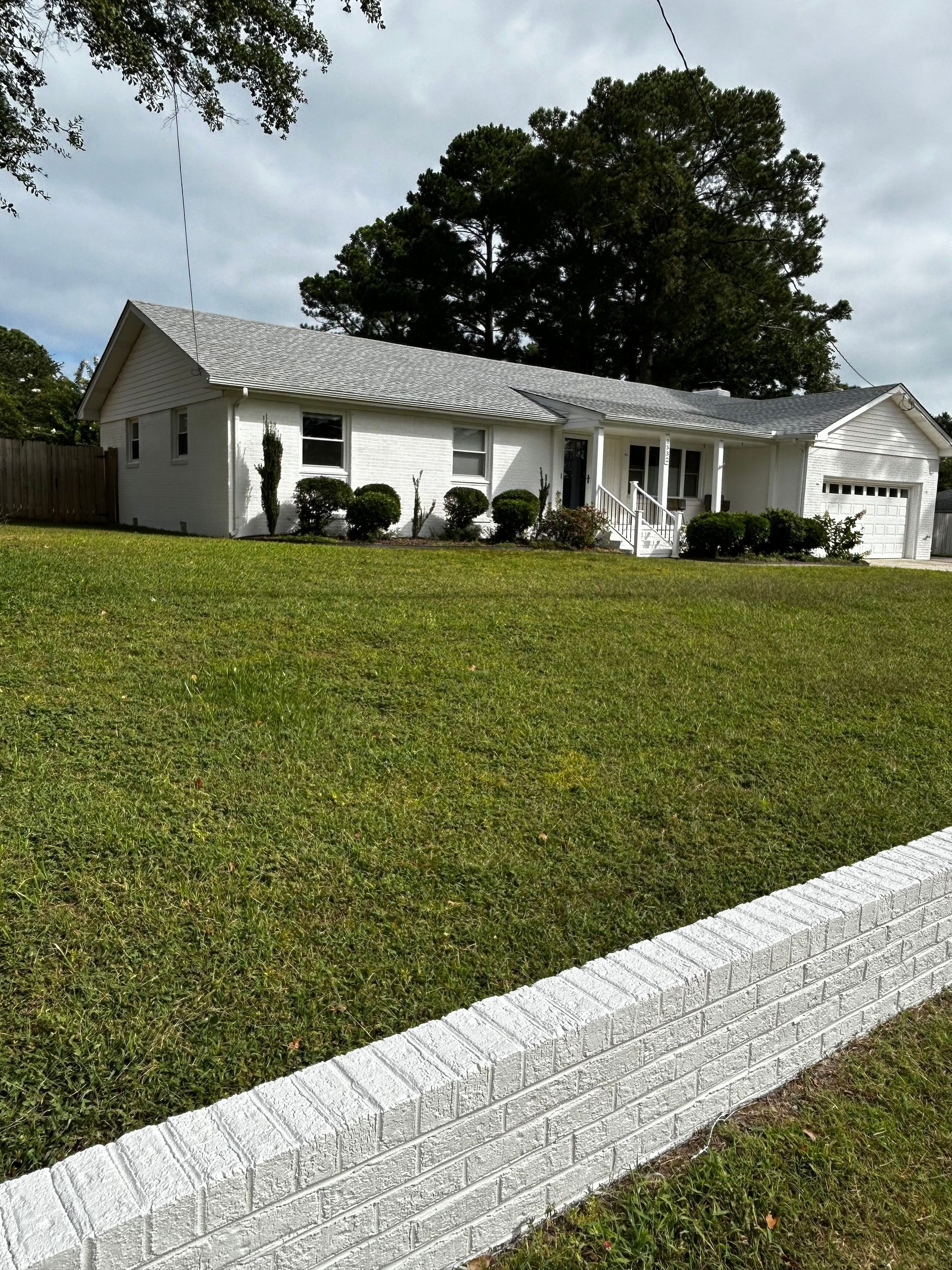 White house with gray roof and green lawn behind a white brick wall.
