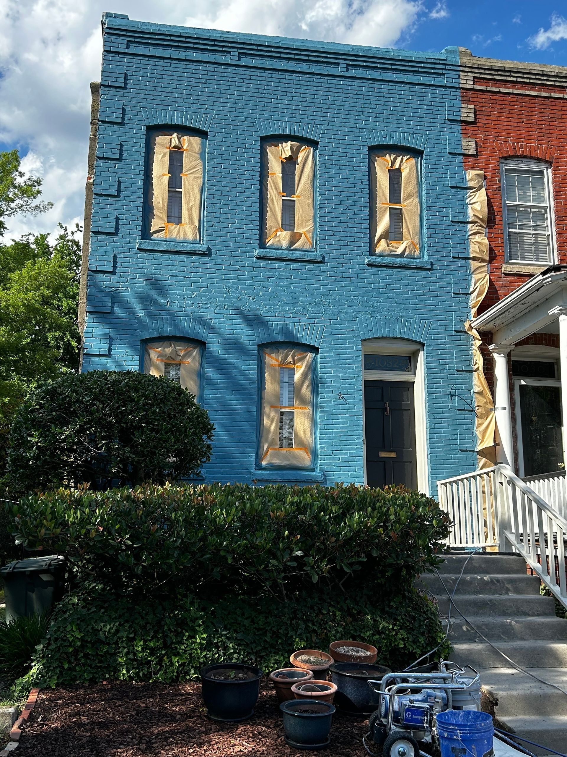 Blue brick building with boarded-up windows, a black door, and a green bush.