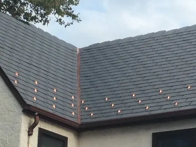 Roof with dark gray shingles and small orange lights along the ridge on a house exterior
