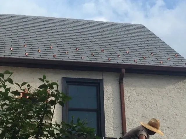 House roof and window with a person in a straw hat working near the wall