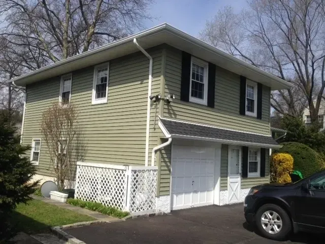 Two-story beige house with green shutters, white garage, and black car parked in front