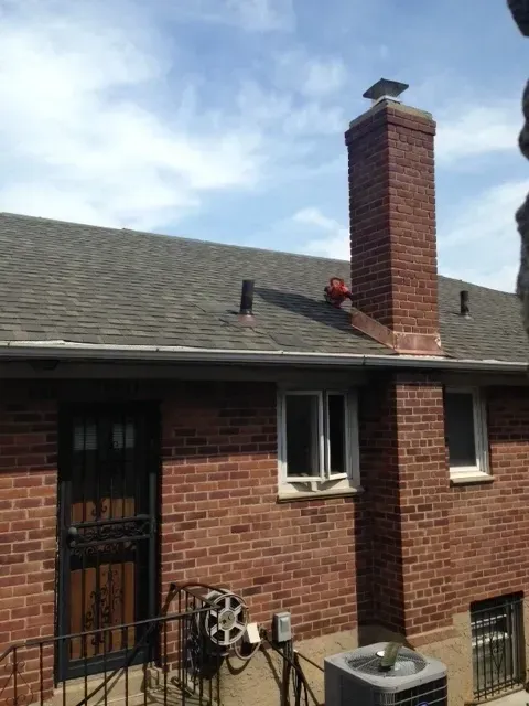 Brick house exterior with chimney, dark roof, metal security door, and utility meters outside under a blue sky