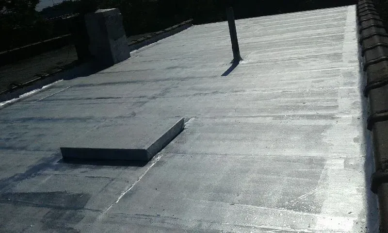 Flat roof with a small rectangular vent and a vertical pipe in bright sunlight.