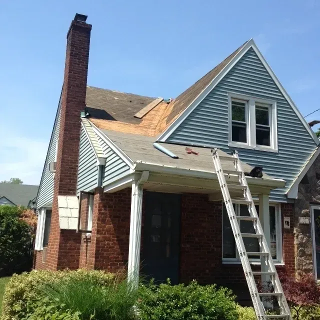 Damaged house with ladder leaning against blue siding and brick chimney under repair