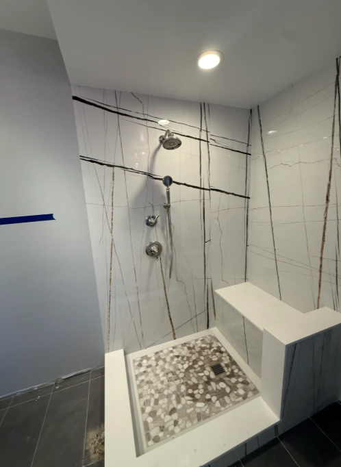 Modern tiled walk-in shower with mosaic floor, glass door, and chrome shower fixtures