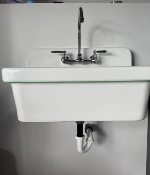 White wall-mounted bathroom sink with chrome faucet and visible drain pipe underneath