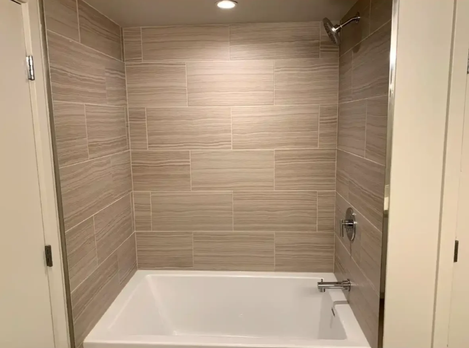 Modern beige-tiled bathtub alcove with recessed lights and white tub