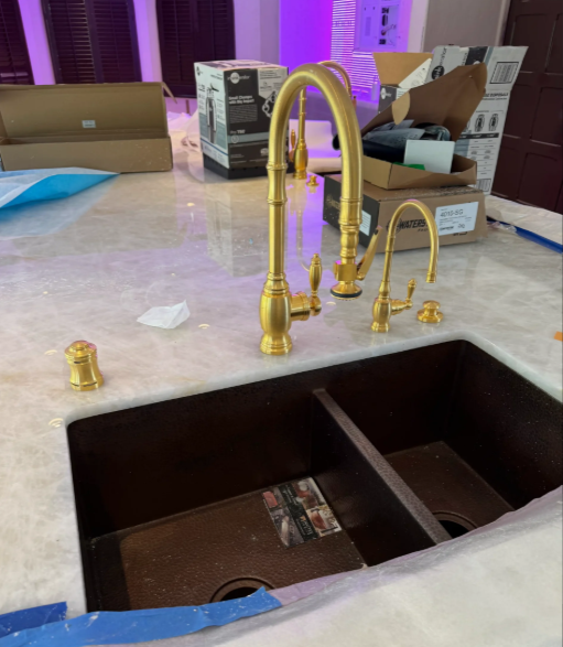 Brass kitchen faucet over dark double sink on a marble countertop with installation parts nearby