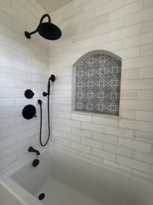 White tiled shower with matte black fixtures and a patterned arched window niche.
