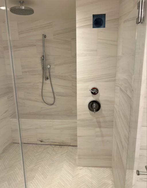 Modern beige tiled walk-in shower with handheld showerhead and built-in controls