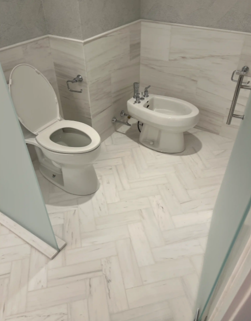 Accessible bathroom with toilet, bidet, and grab bars on white tiled floor and walls