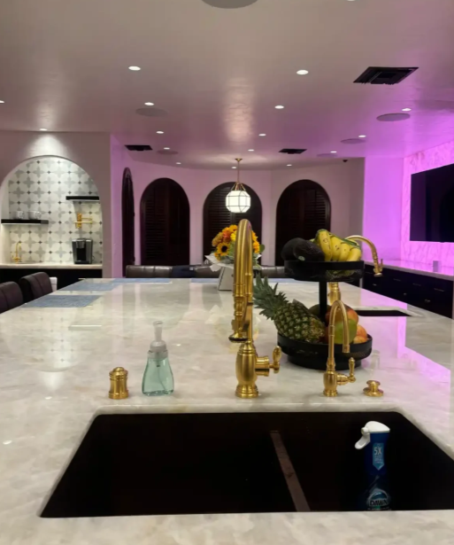 Modern kitchen with white island, gold faucet, black sink, and purple accent lighting