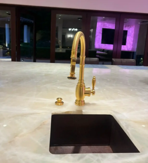 Gold faucet over a black sink on a light marble countertop in a modern bathroom