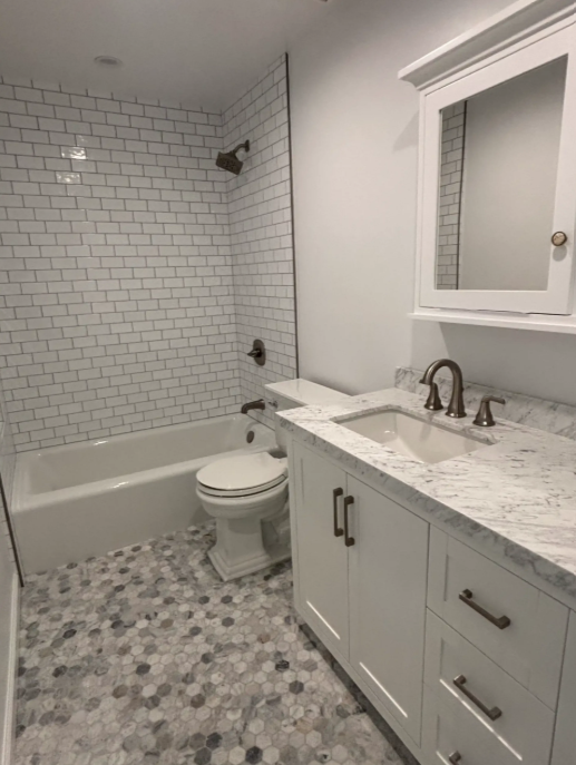Modern bathroom with white subway tile shower, gray vanity, marble countertop, and patterned tile floor