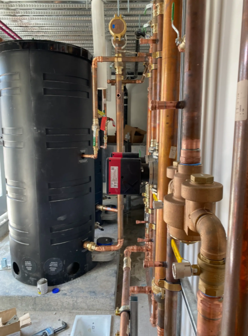 Mechanical room with black tank, red pump, and copper pipes along a wall