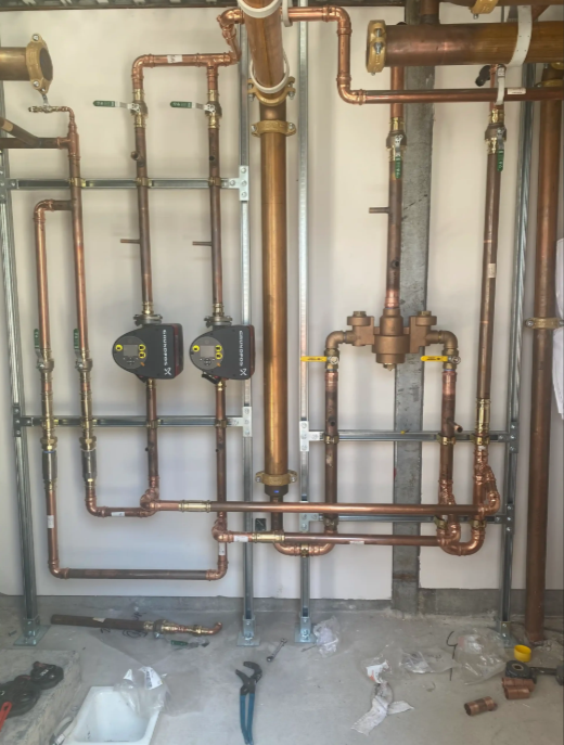 Copper plumbing pipes and two black pumps on a wall in an unfinished utility room