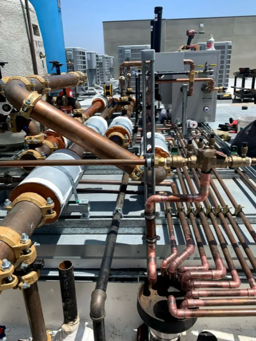 Rooftop HVAC and plumbing pipes with copper lines, valves, and insulated ducts in an industrial setting