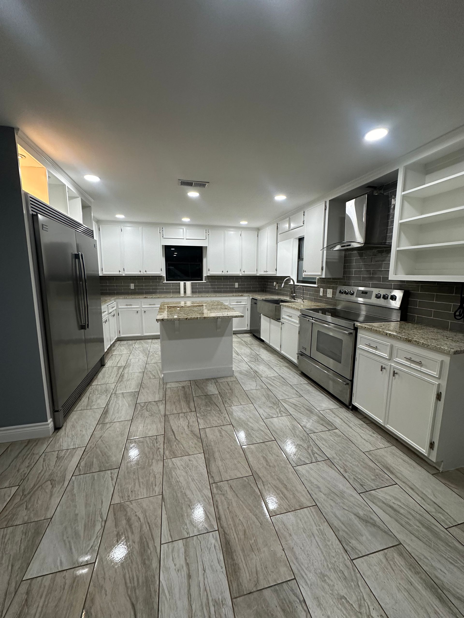 White kitchen with stainless steel appliances, gray countertops, and tile flooring.