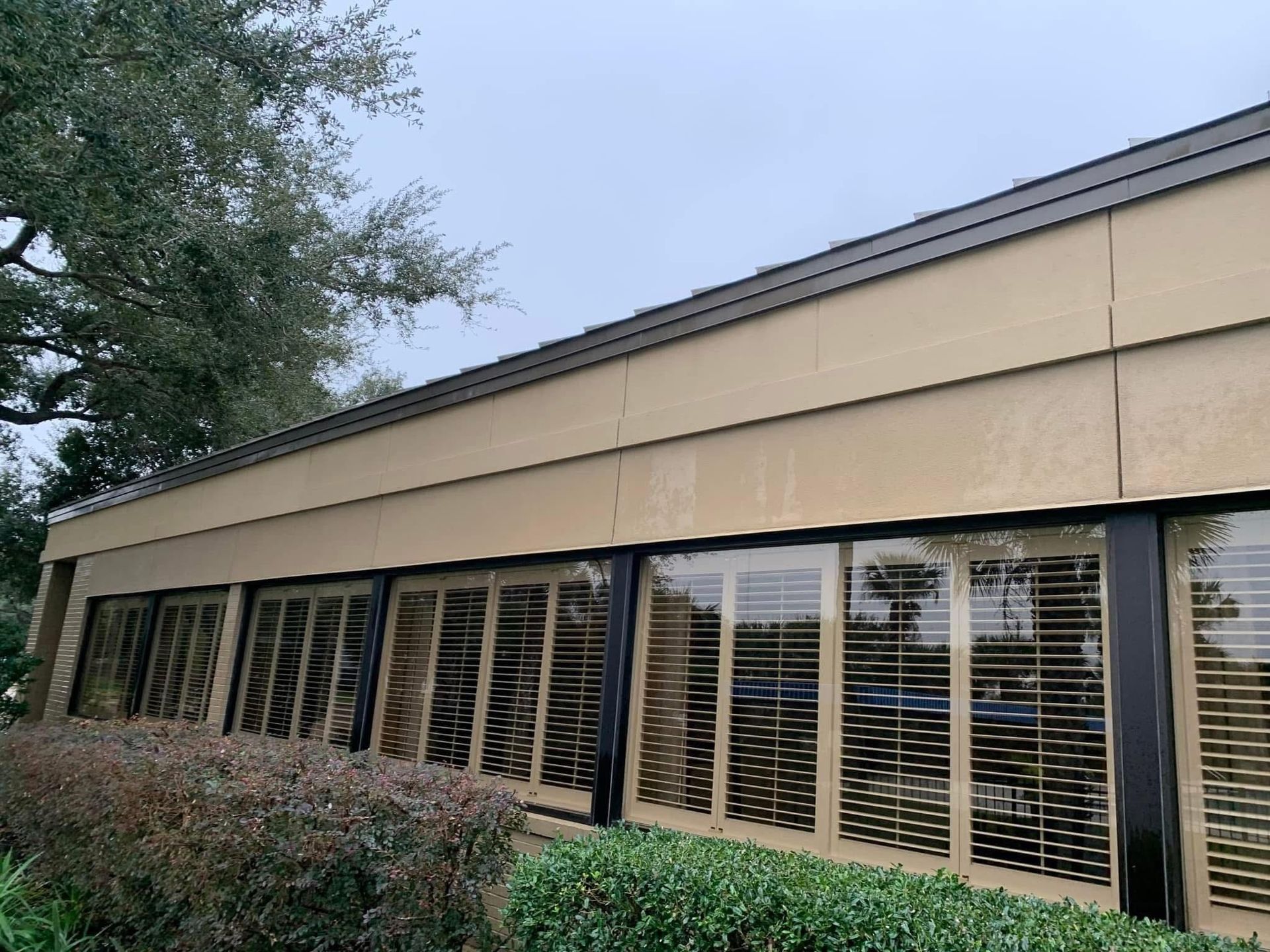 Exterior view of a tan commercial building with large windows and closed blinds. Overcast sky.
