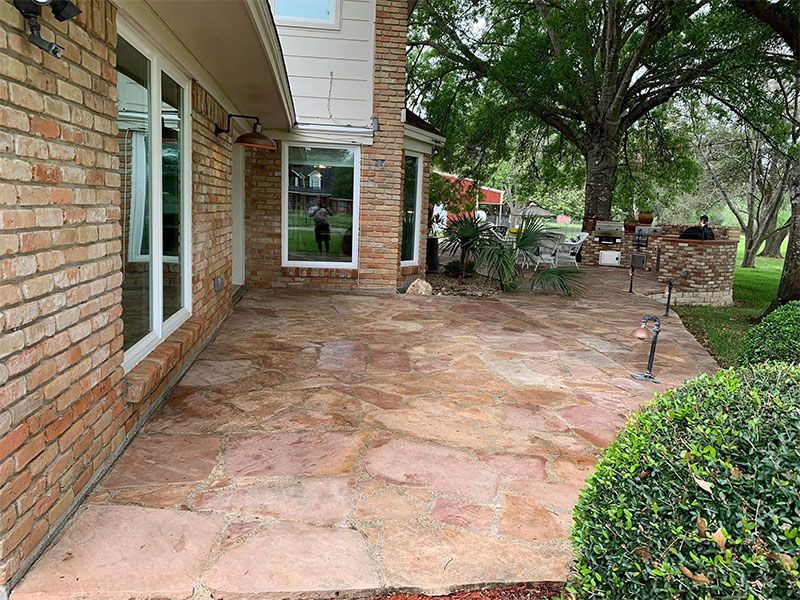 Brick house with flagstone patio. Green shrubs and trees in the yard.