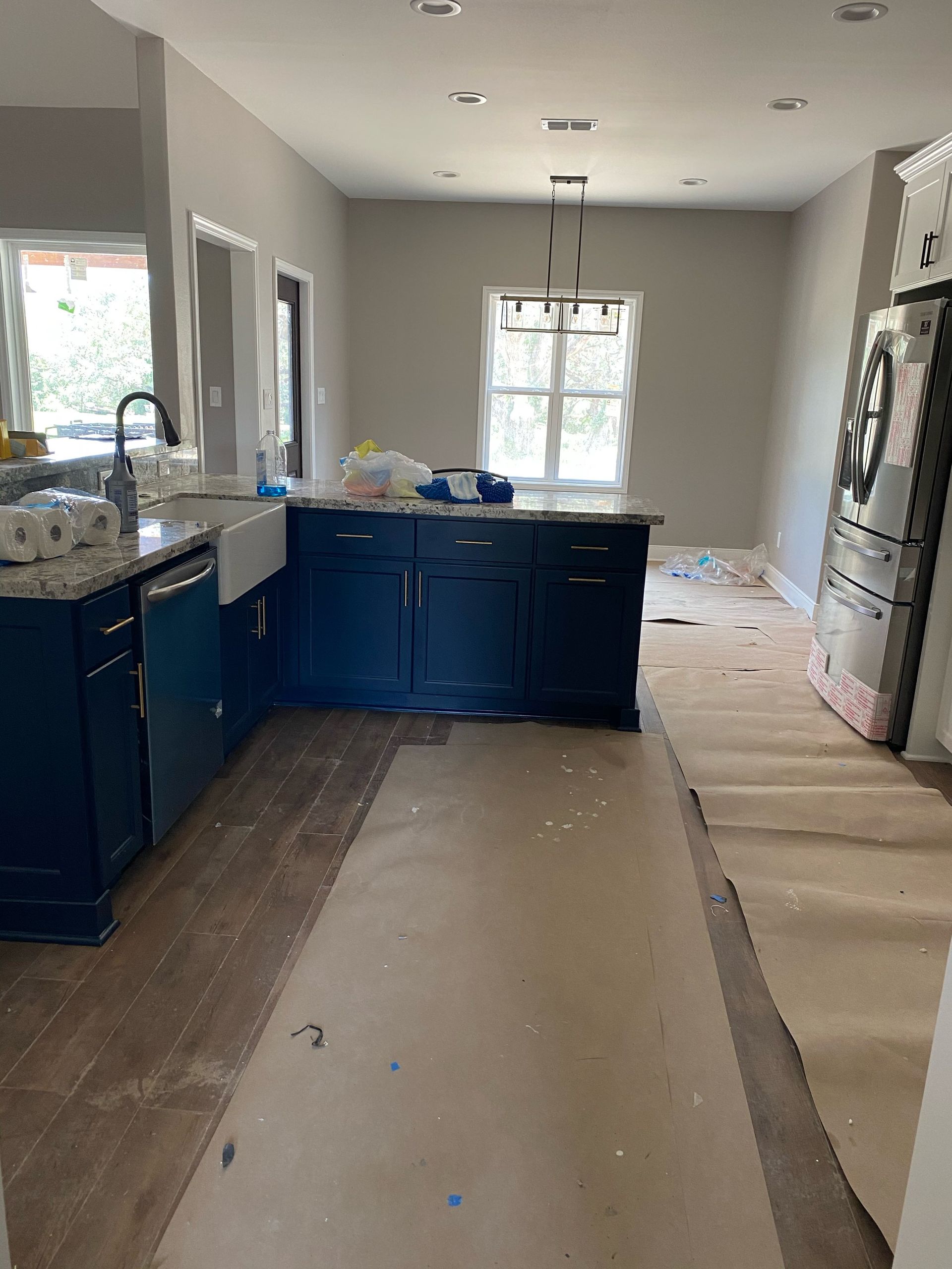 Kitchen with navy blue cabinets, white farmhouse sink, and an island. Brown paper covers the floor.