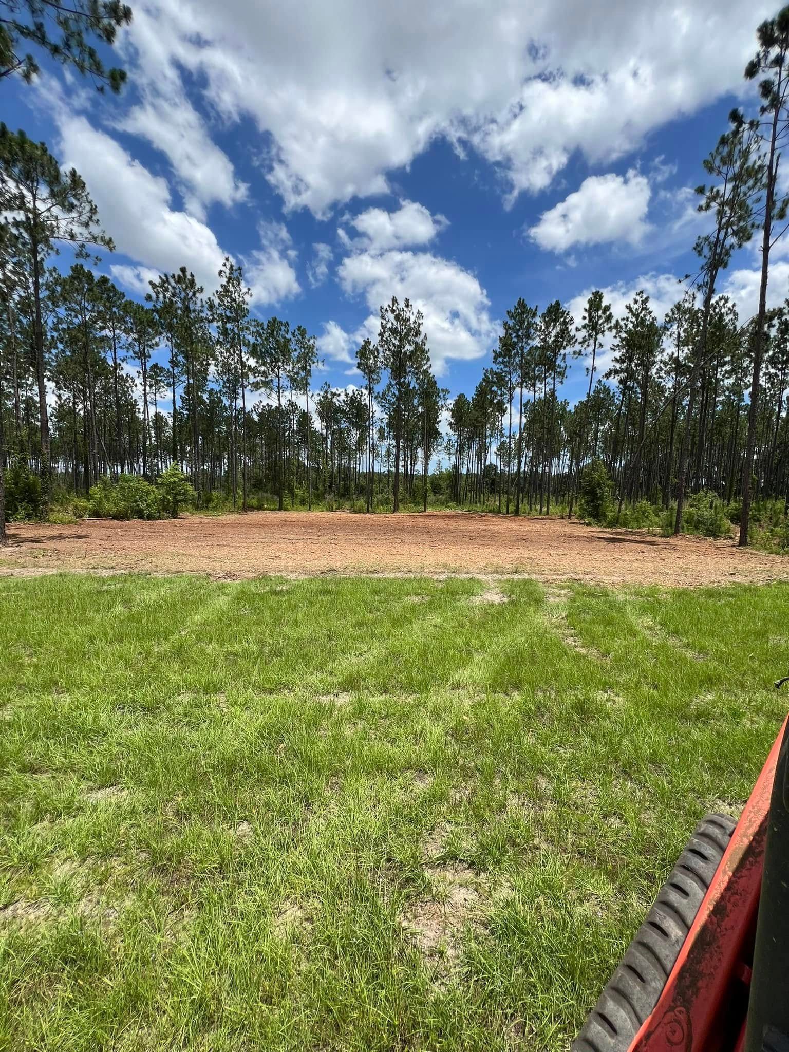 A person is mowing a lush green field with trees in the background.
