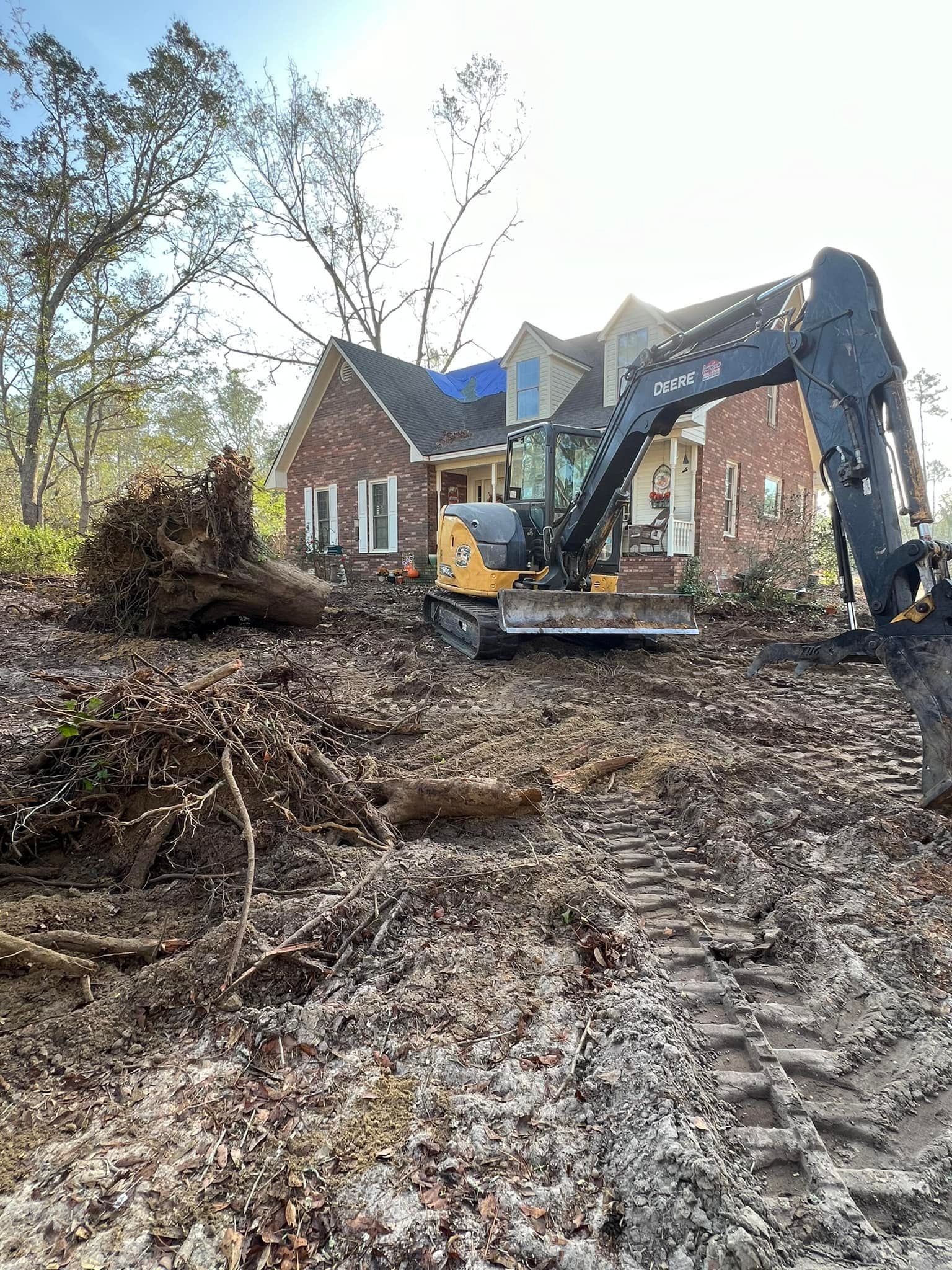 A large excavator is moving dirt in front of a brick house.