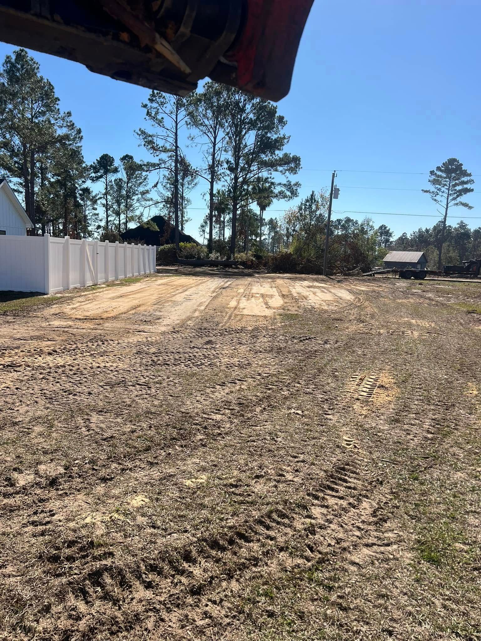 A dirt road with a white fence and trees in the background.