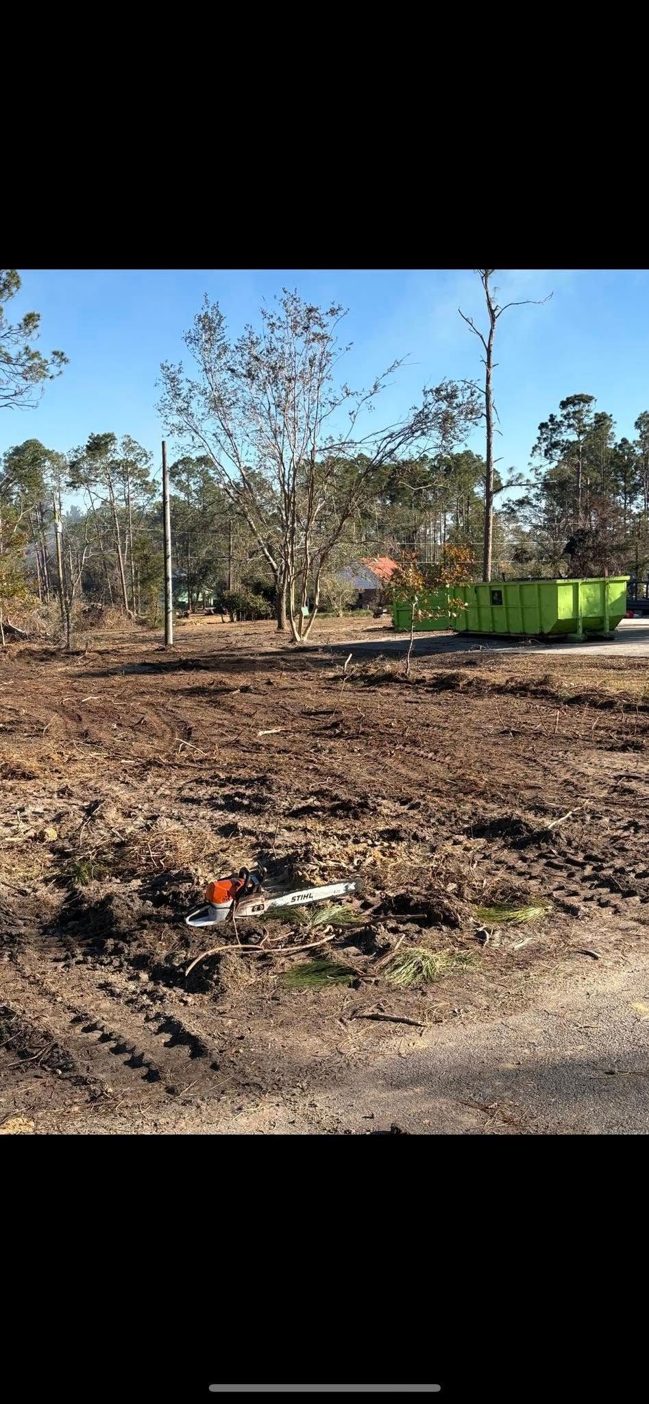 There is a green dumpster in the middle of a dirt field.