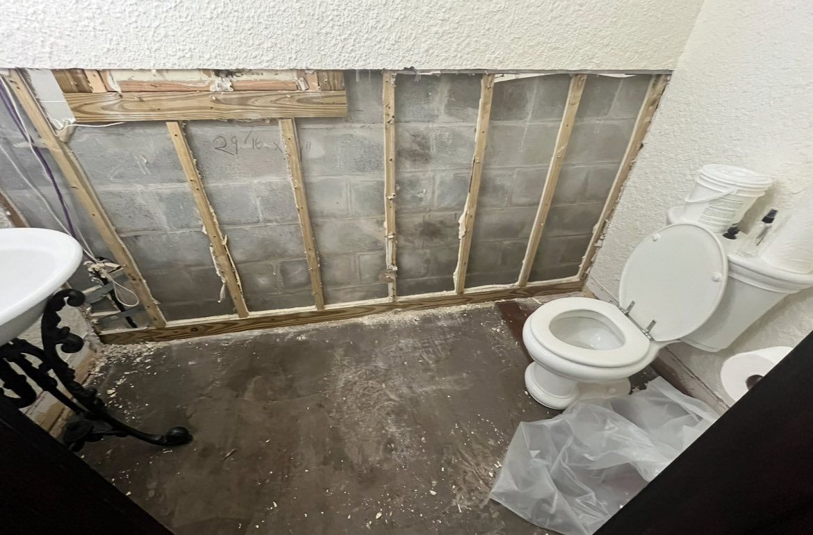 Bathroom renovation: exposed cinder block wall, toilet, sink, debris on floor.