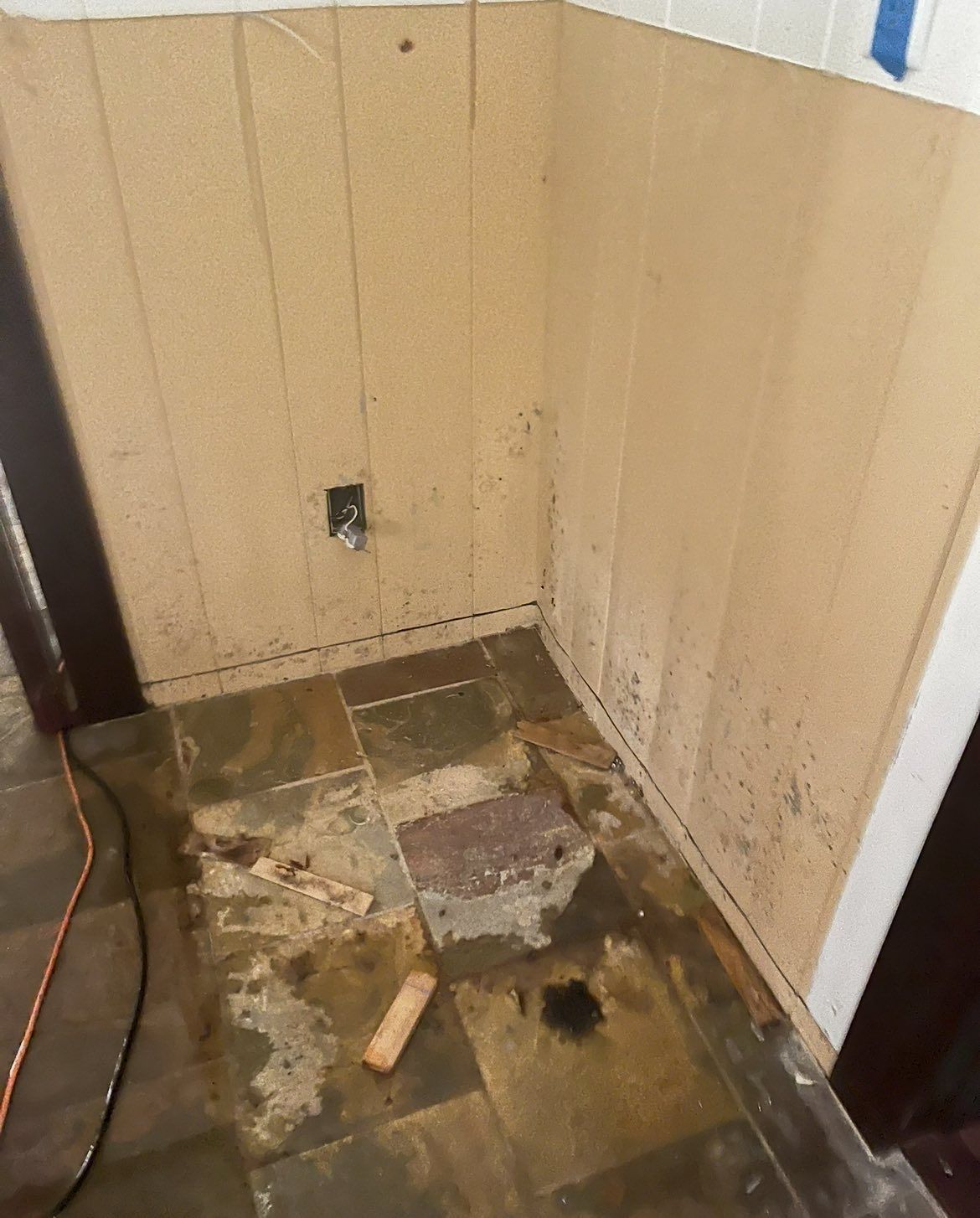 Bathroom with water damage on the wall and floor, showing discoloration and a faucet.