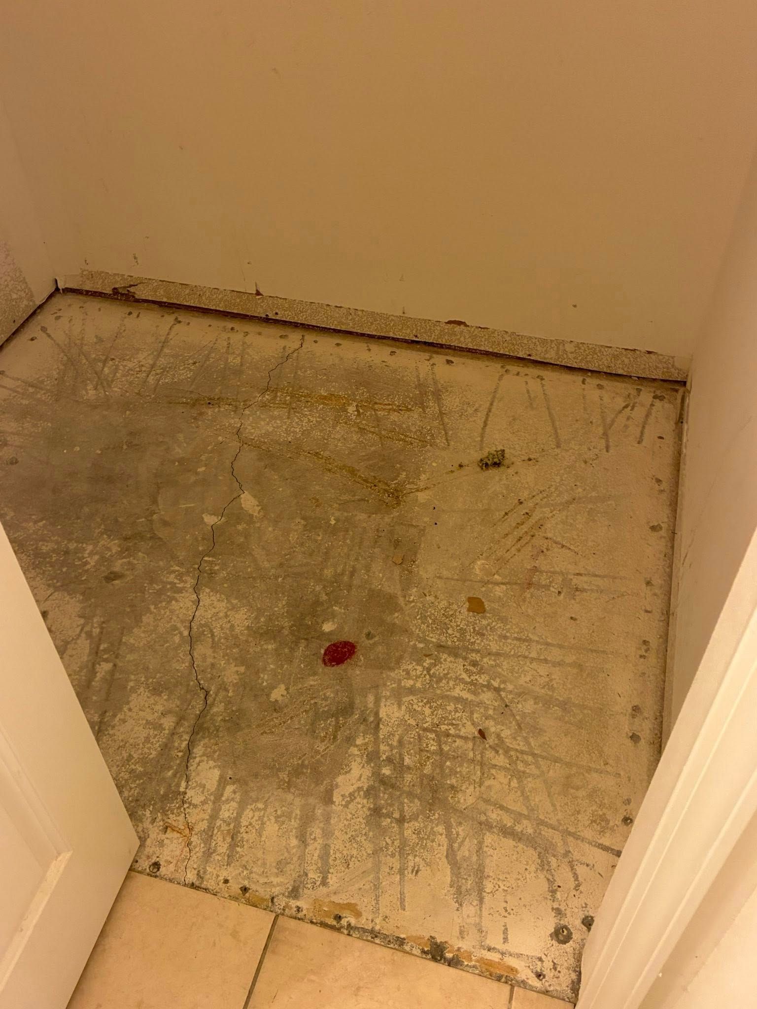 Bare, stained concrete floor in a small alcove. The floor shows remnants of adhesive and water damage.