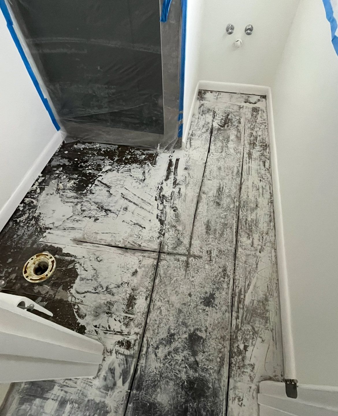 Bathroom renovation in progress: floor covered in debris and white material, shower area taped off.