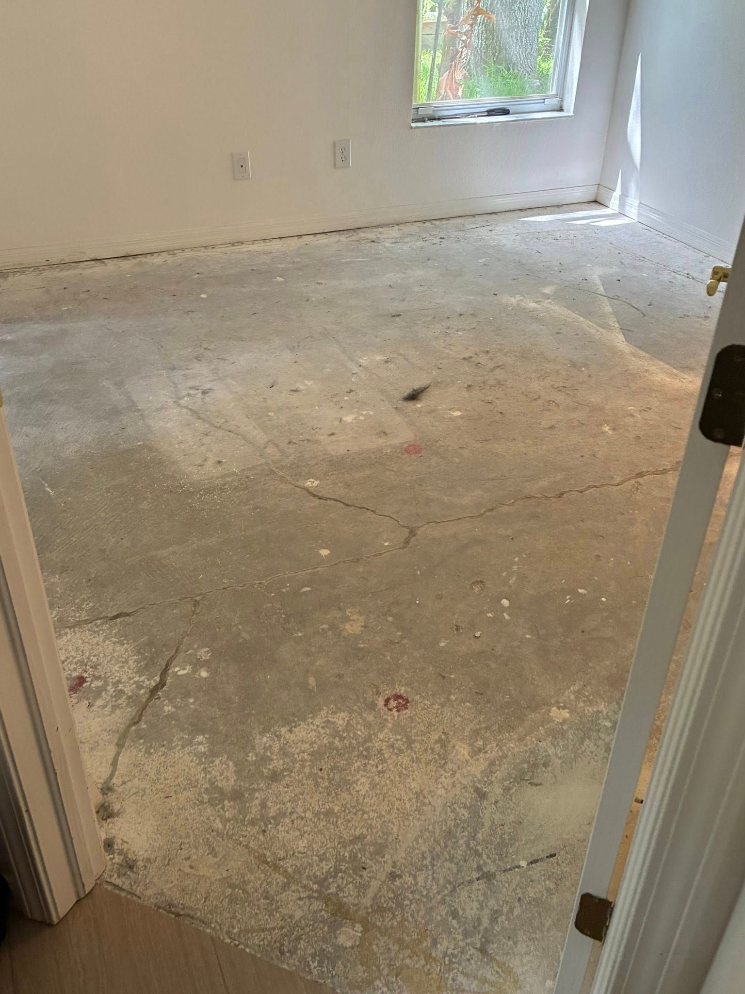 Bare concrete floor in a room, with white paint flecks and cracks. A door frame is on the right side.