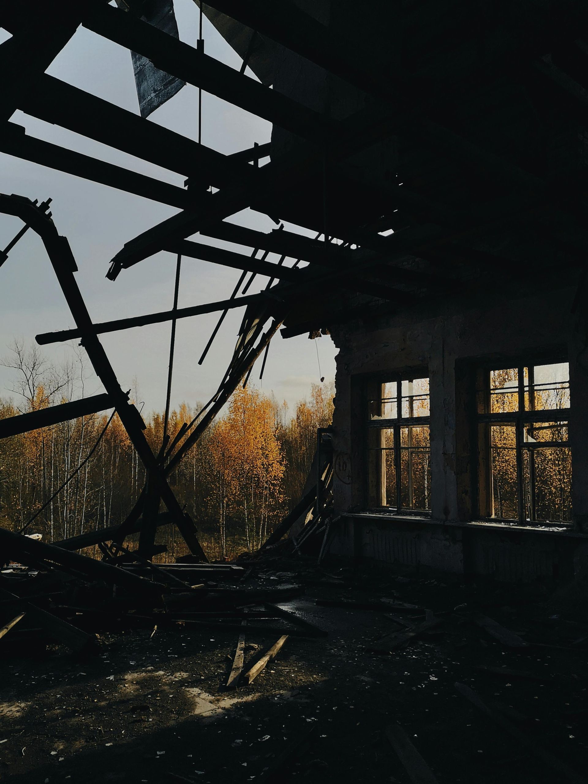 Interior of a burnt-out building; view through windows of autumn trees, dark, decayed, and damaged.