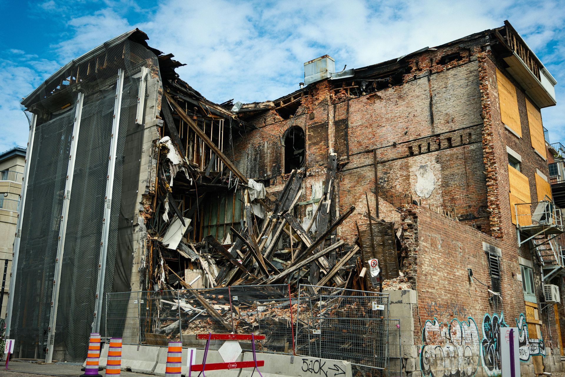 Damaged brick building with exposed wooden beams, remnants of fire, and boarded windows.
