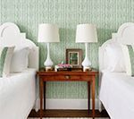 Two white beds with lamps and a wooden table against green textured wallpaper.
