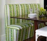 Green-striped upholstered dining bench with a wooden table, glasses, and white plates.