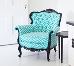 Turquoise patterned armchair with ornate black frame. Side table next to the chair.