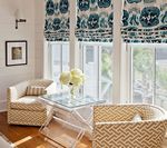 Two armchairs facing each other by a window with patterned Roman shades, glass table, and flowers.