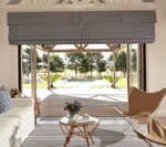 Living room with open doors to a patio. Blue patterned window shade, white couch, light brown chair, outdoor view.