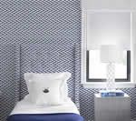Bedroom with blue patterned wallpaper, white bed, nightstand, and window with blinds.